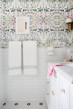 a bathroom with floral wallpaper and white tile flooring, two towels hanging on the rack