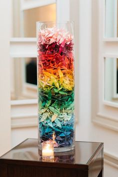 a tall vase filled with lots of different colored flowers on top of a wooden table