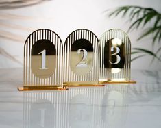 three golden numbers are placed next to each other on a white table with a plant in the background