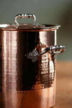 a large copper pot sitting on top of a wooden table next to a metal spoon