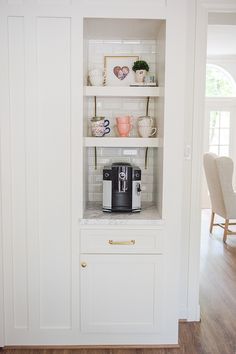 a kitchen with white cupboards and shelves filled with coffee cups on top of them