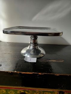 a metal cake plate sitting on top of a wooden table next to a white wall