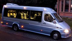 a silver bus is parked on the side of the road with its lights turned on