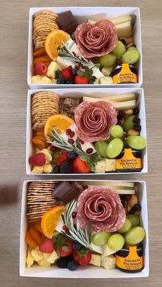 two white boxes filled with assorted fruit and crackers on top of a wooden table