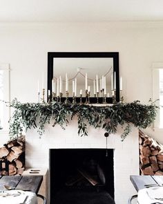 the fireplace is decorated with greenery and candles in front of an empty dining table