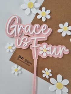 a cake topper that says grace is fun with daisies on the table next to it