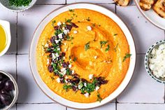 a bowl of hummus with olives, pita bread and other foods on the side