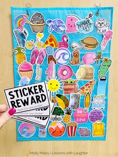 a person holding up a sticker reward in front of a wooden table with an assortment of stickers on it