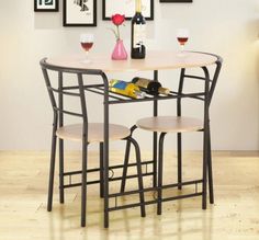 a small table with two chairs and bottles of wine on top of it in front of pictures hanging on the wall