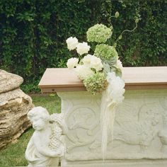 a vase with white flowers sitting on top of a stone bench next to a statue