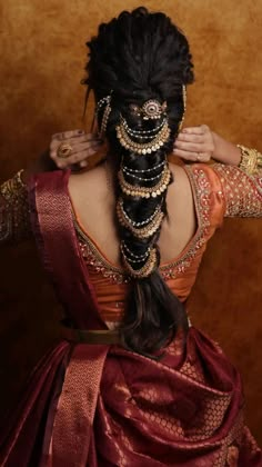 a woman with long black hair wearing a red and gold saree, braided into a ponytail