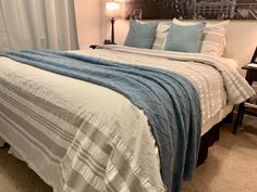 a bed with blue and white comforter on top of it next to a night stand