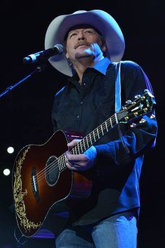 a man wearing a cowboy hat and holding a guitar in front of a microphone on stage