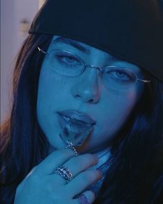 a woman wearing glasses and a beanie poses for the camera with her hand on her chin