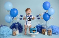 a baby boy standing in front of blue and white decorations with his first birthday cake