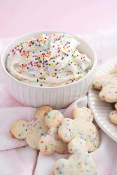 some cookies and white frosting in a bowl with sprinkles on the table