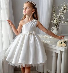 Presenting a stunning one-shoulder satin flower girl dress that captures the essence of elegance and innocence. Perfect for weddings, communions, baptisms, or any formal occasion, this knee-length dress is designed to make your little one shine on her special day. The dress features a graceful one-shoulder design, adorned with a delicate bow that adds a touch of sophistication. The bodice seamlessly transitions into a voluminous skirt with a tulle overlay, creating a soft and ethereal silhouette One Shoulder Flower Girl Dress, Satin Dresses For Kids, Dress With Tulle Overlay, Toddler Wedding Dress, African Kids Clothes, Holy Communion Dresses, Satin Flower Girl Dress, Wedding Dresses For Kids, Voluminous Skirt