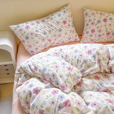 an unmade bed with flowers on it and two pillows in the foreground, next to a night stand