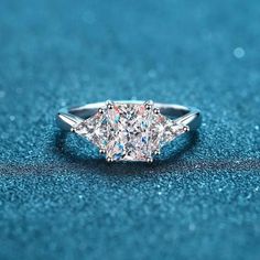 an engagement ring with three princess cut diamonds on the top and bottom, sitting on a blue surface