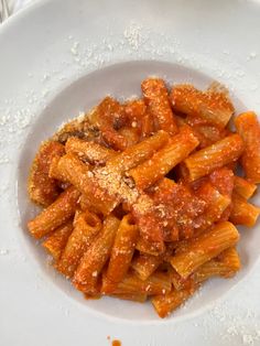 pasta with sauce and parmesan cheese in a white bowl on top of a table