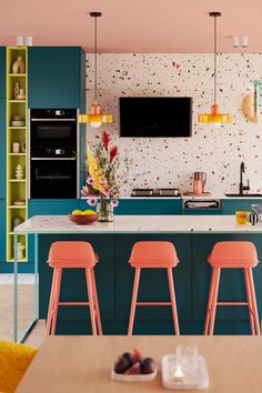 a kitchen with blue cabinets and pink stools next to a counter top that has flowers on it