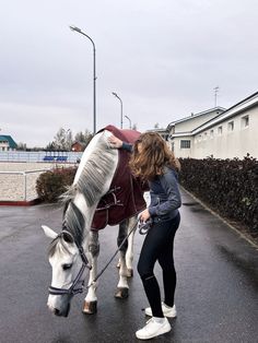 a woman standing next to a white and gray horse on a street with buildings in the background