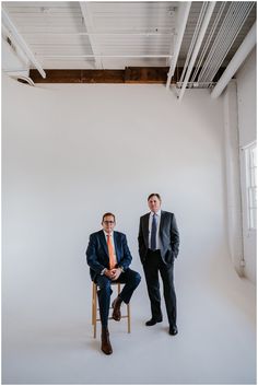 two men in suits and ties are posing for the camera while one man is sitting on a chair