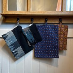 three pieces of cloth hanging from hooks on a wall next to a mirror and shelf