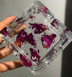 a hand holding a square glass container filled with ice and red flowers on top of it