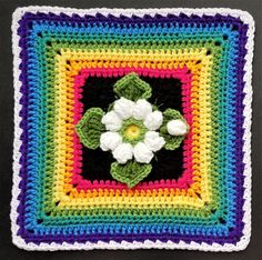 a crocheted square with a flower on it in multicolors and white