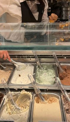 an ice cream shop employee scooping out gelato from trays in front of the counter