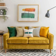 a living room with yellow couches and green pillows on the floor next to a painting