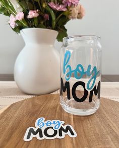 a glass with the word boy mom on it next to a vase with flowers in it