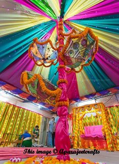 an umbrella decorated with flowers and garlands in front of colorful drapes at a wedding