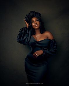 a woman in a black dress posing for the camera with her hand on her head