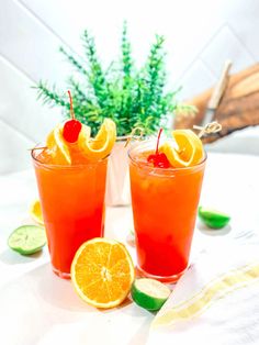 two glasses filled with orange juice, garnished with cherries and limes