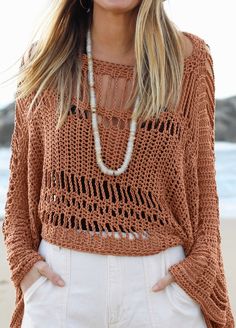 a woman standing on top of a beach next to the ocean wearing a brown sweater and white shorts