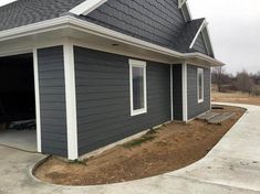 a gray house with white trim on the roof and two windows in the garage area