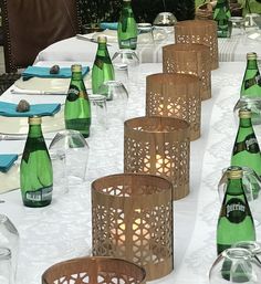 a table topped with lots of green bottles and glasses next to candles on top of a white table cloth