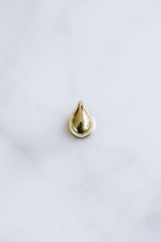 a small gold tear shaped object on a white surface