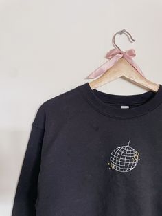 a black sweatshirt with an embroidered globe on the front and pink ribbon around the neck