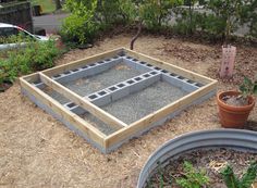 a garden area with plants and cement blocks in the ground next to potted plants