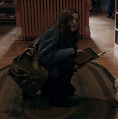 a woman kneeling down on the floor with a book in her hand and looking at it