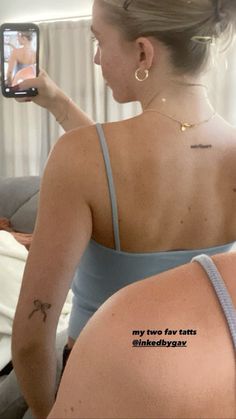 a woman taking a selfie in the mirror with her cell phone and tattoos on her back