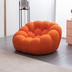 an orange bean bag chair sitting on top of a floor next to a dresser and window