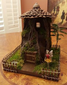 a fairy house made out of wood and moss with a tinkerbell figurine