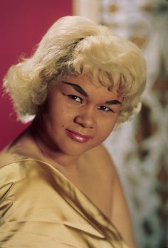 a close up of a person wearing a gold dress and posing for a photo with her hair pulled back