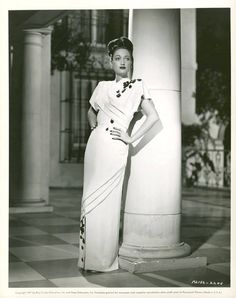 an old black and white photo of a woman in a dress standing next to columns