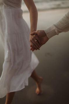 two people holding hands while walking on the beach