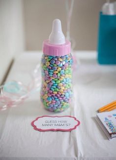 a baby bottle filled with lots of colorful candies next to a note and pencils